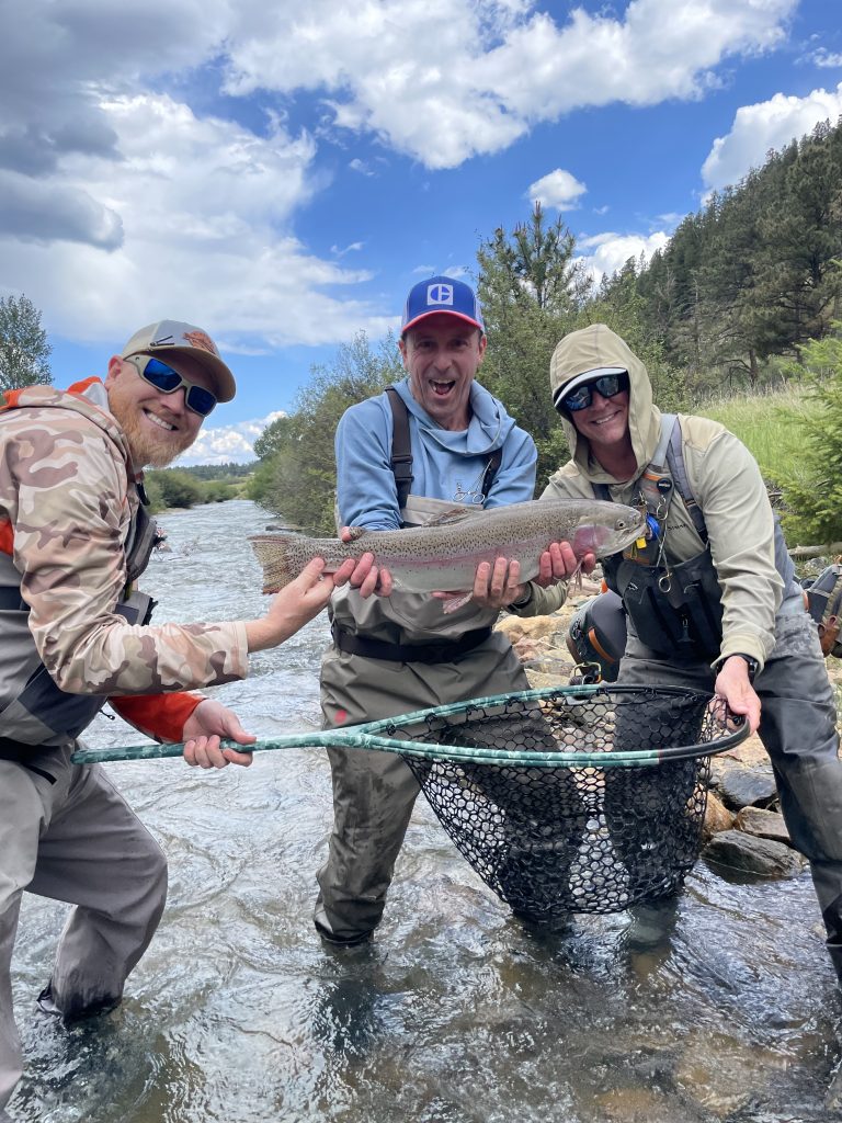 Everything You Never Wanted to Know About Fly Fishing Nets, Three men hold fish in a river that was caught with fly fishing net